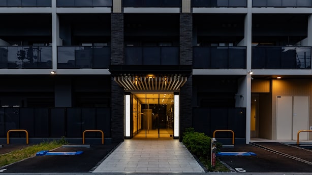 A modern building with a central entrance, multiple balconies, and a gated parking area.