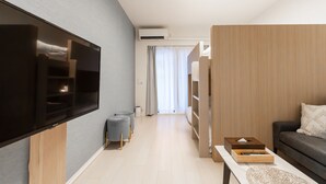 A modern living room with a flat-screen TV, a grey sofa, a wooden coffee table, and a wooden wardrobe.