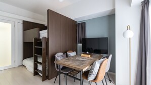 A compact room with a dining table, chairs, a TV, a wardrobe, and a floor lamp.