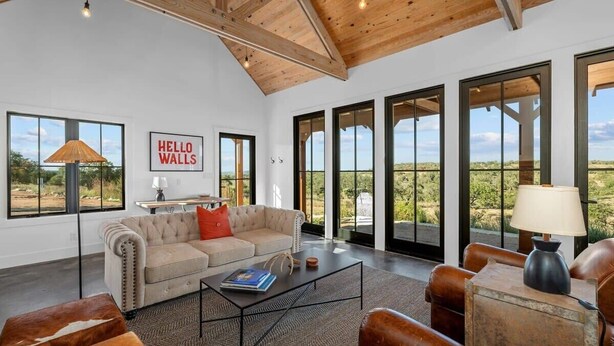 A spacious living room with a high ceiling, large windows, and a view of the desert landscape. - Hello Walls, Hot tub, Hill Country Views (Fredericksburg)