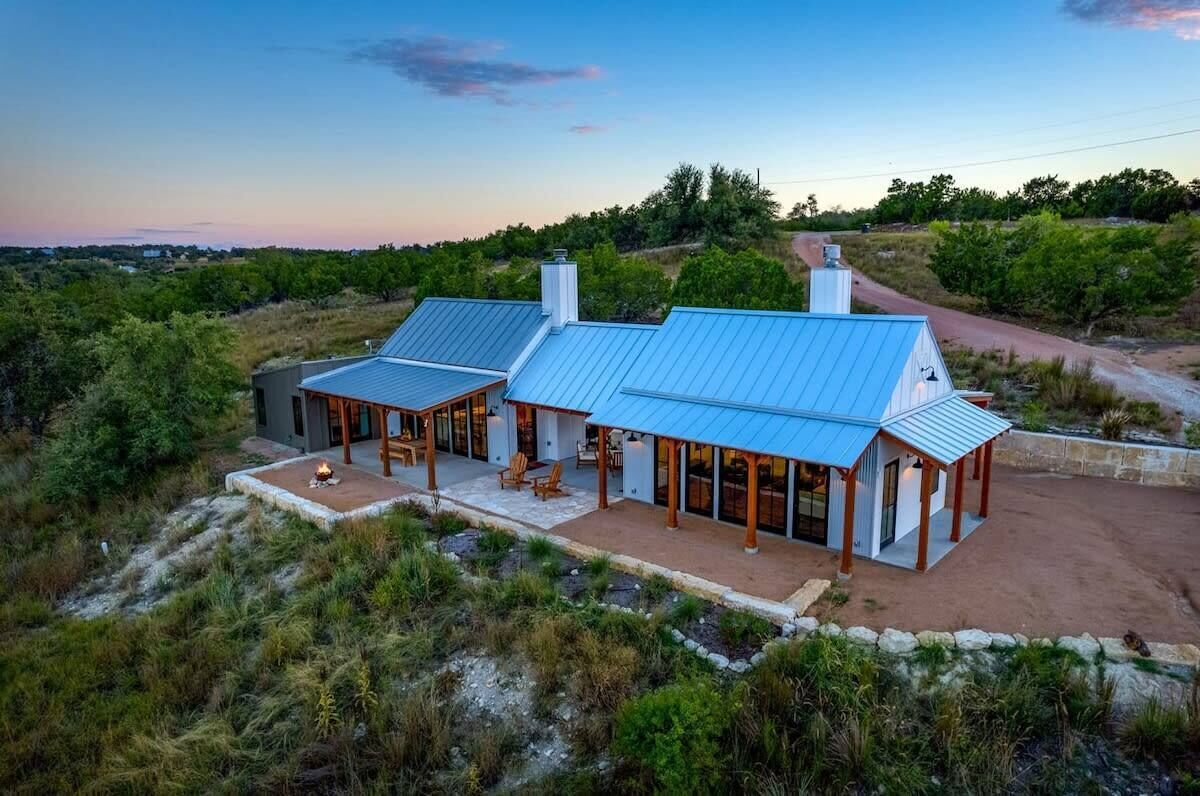 A modern two-story house with a blue metal roof, large glass windows, and a stone pathway leading to the entrance.