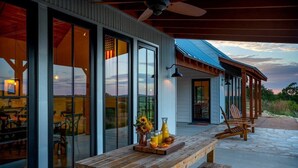 A modern house with large glass doors, a wooden deck, and a patio area with a table set for breakfast. - Hello Walls, Hot tub, Hill Country Views (Fredericksburg)