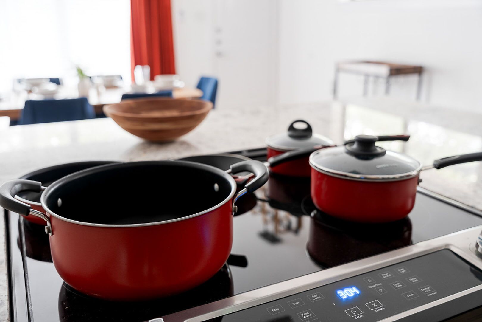 A modern kitchen with a stovetop, two red pots, and a digital control panel.