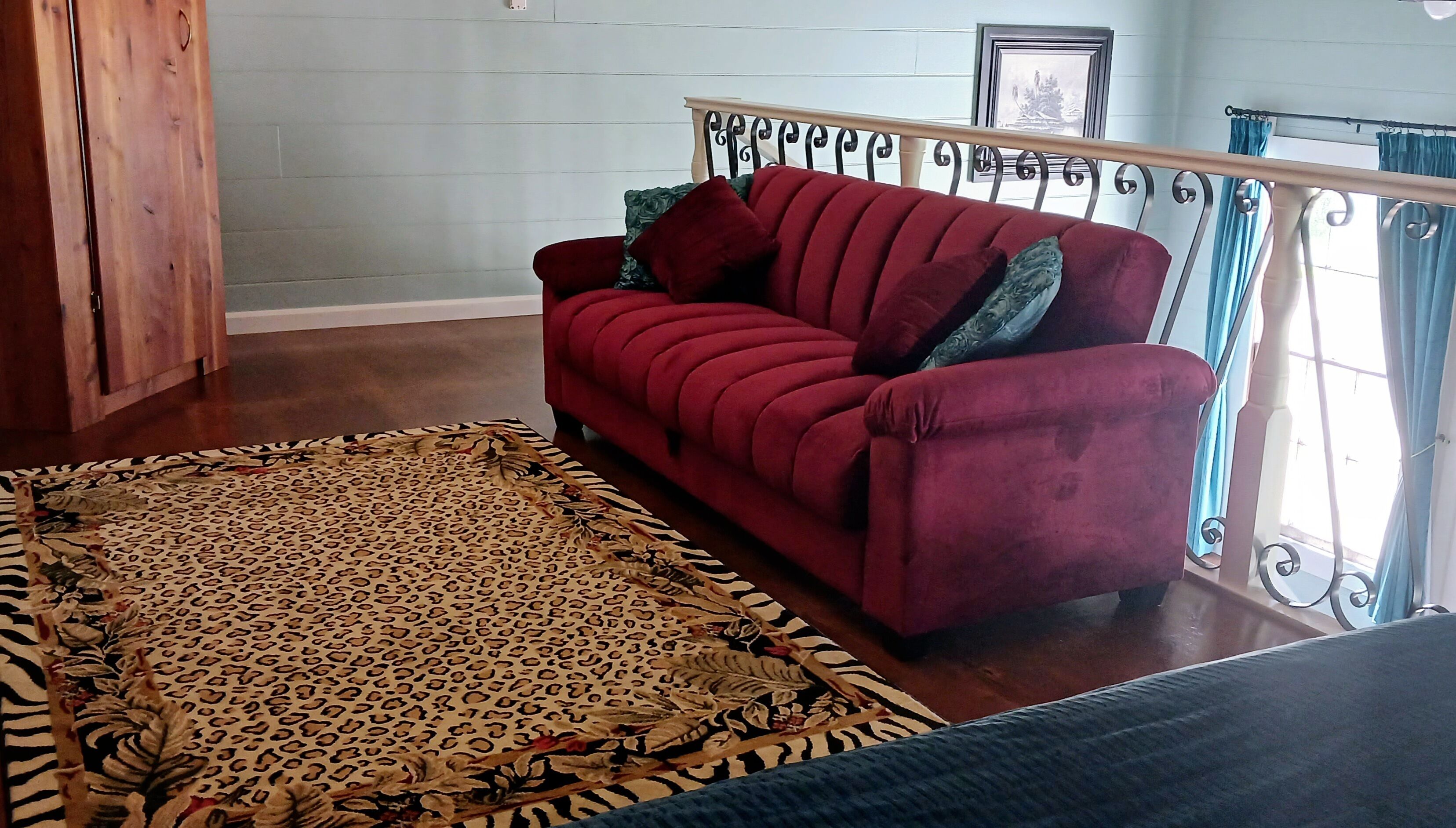 A red sofa with patterned cushions, a leopard print area rug, and a staircase with metal railings.