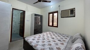 Une chambre à coucher comprenant un lit, un ventilateur de plafond, une fenêtre avec des stores et un climatiseur fixé au mur.