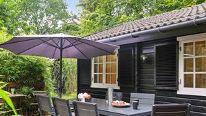 An outdoor dining area with a table and chairs, a purple umbrella, and a house with black shutters and a tiled roof. - "Neela" - 300m from the sea by Interhome (Væggerløse)