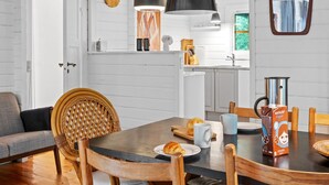 A modern kitchen with white wooden walls, a dining table with chairs, a hanging light fixture, and a clock on the wall. - "Neela" - 300m from the sea by Interhome (Væggerløse)
