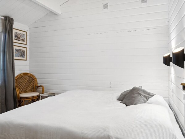 A bedroom with a large bed, a wicker chair, and a nightstand.