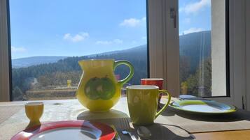 Ein Tisch ist gedeckt mit Tellern, einer Karaffe und Tassen, mit Blick auf eine malerische Berglandschaft durch ein Fenster.