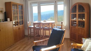 A dining area with a table and chairs, a large window with a view of the outdoors, and wooden cabinets. - Oberwiesenthal, Unweit der Skipiste (Oberwiesenthal)
