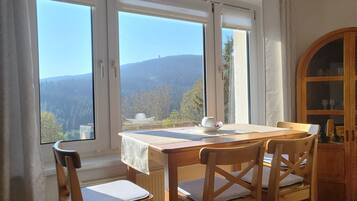 Ein Essbereich mit Tisch und Stühlen, große Fenster mit Blick auf Berge und Bäume sowie ein Holzkabinett.