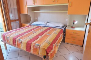 Un lit avec une couverture colorée, une lampe de chevet et une petite commode.