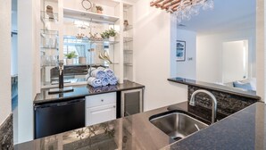 A modern kitchen with a black countertop, stainless steel sink, and a wooden ceiling with hanging glassware. - ATX Oasis retreat - pool, hot tub, games & more! Trendy modern setup. (Austin)