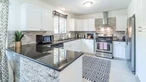 A modern kitchen with white cabinets, a granite countertop, stainless steel appliances, and a patterned rug. - ATX Oasis retreat - pool, hot tub, games & more! Trendy modern setup. (Austin)