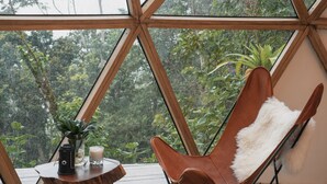 A room with a large window, a brown chair, a small table with a candle, and a plant. - TERRAMIA ESTATE (Santa Marta)