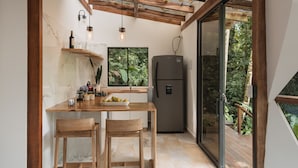 A compact kitchen with a wooden table, two chairs, a refrigerator, and a window overlooking a lush garden. - TERRAMIA ESTATE (Santa Marta)
