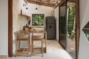 Una cocina compacta con una mesa de madera, dos sillas, un refrigerador y una ventana con vistas a un jardín exuberante.