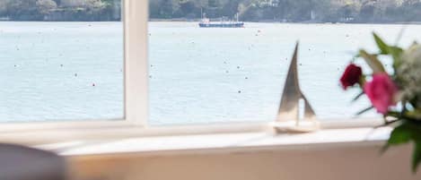 A room with a large window overlooking a lake, a desk, and a chair.