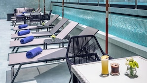 Área de piscina en la azotea con sillones de descanso, sombrillas y una mesa con bebidas.