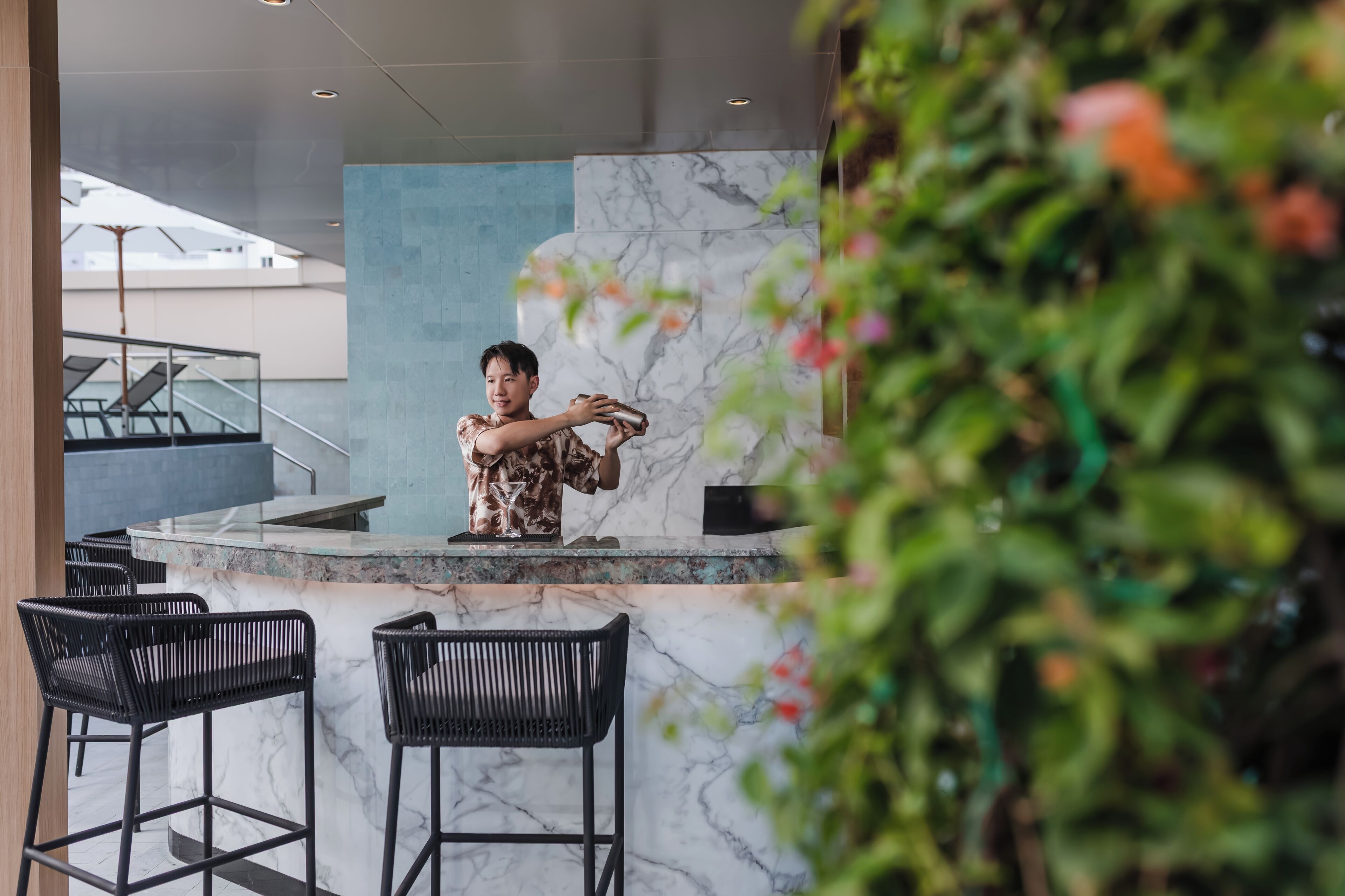 Eine moderne Bar mit Marmorplatten, schwarzen Barhocker und einer Treppe im Hintergrund.