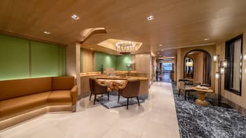A modern hotel lobby with a curved sofa, a dining area with a chandelier, and a marble floor.
