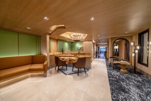 Un moderno vestíbulo de hotel con un sofá curvo, una zona de comedor con candelabro y un suelo de mármol.