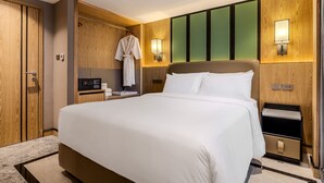 Habitación de hotel con una cama grande, una bata colgada en un perchero, una mesita de noche con una lámpara y un armario de madera.