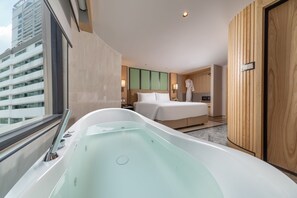 Habitación de hotel moderna con una bañera grande, una cama y vistas a un paisaje urbano.