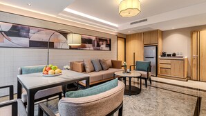 Un saló modern amb un sofà, una taula de centre i una taula de dinar. Hi ha una zona de cuina amb un frigorífic i armaris.
