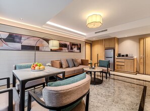 A modern living room with a sofa, coffee table, and dining table. There is a kitchen area with a refrigerator and cabinets. - Samala Suites Bangkok Sukhumvit 19 by Kingston Hotels (Bangkok)