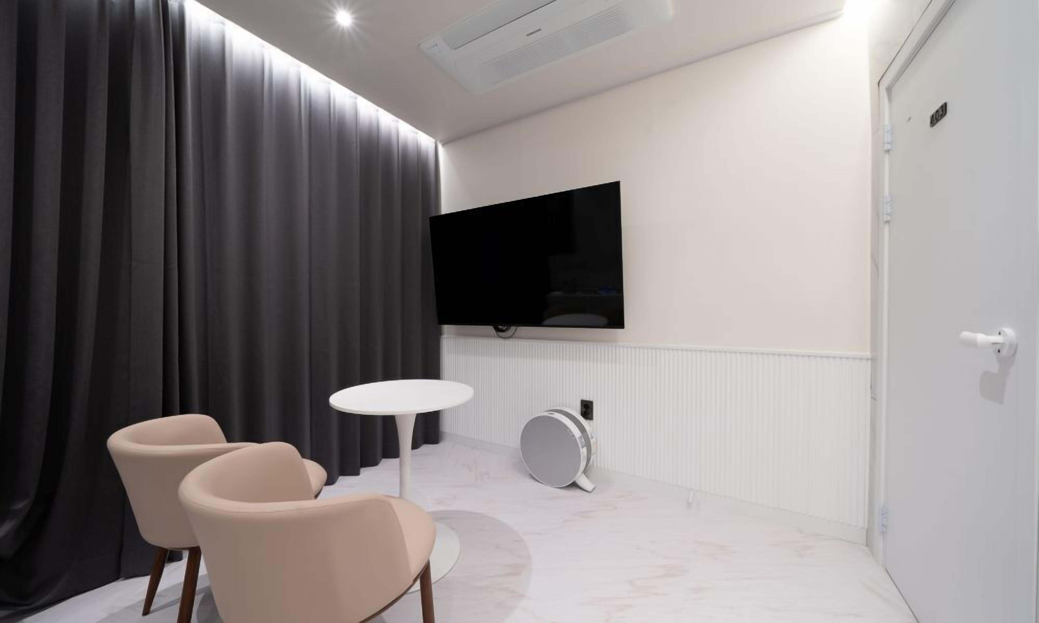 A modern room with a large flat-screen TV mounted on the wall, a round table, two chairs, and a door with a number.