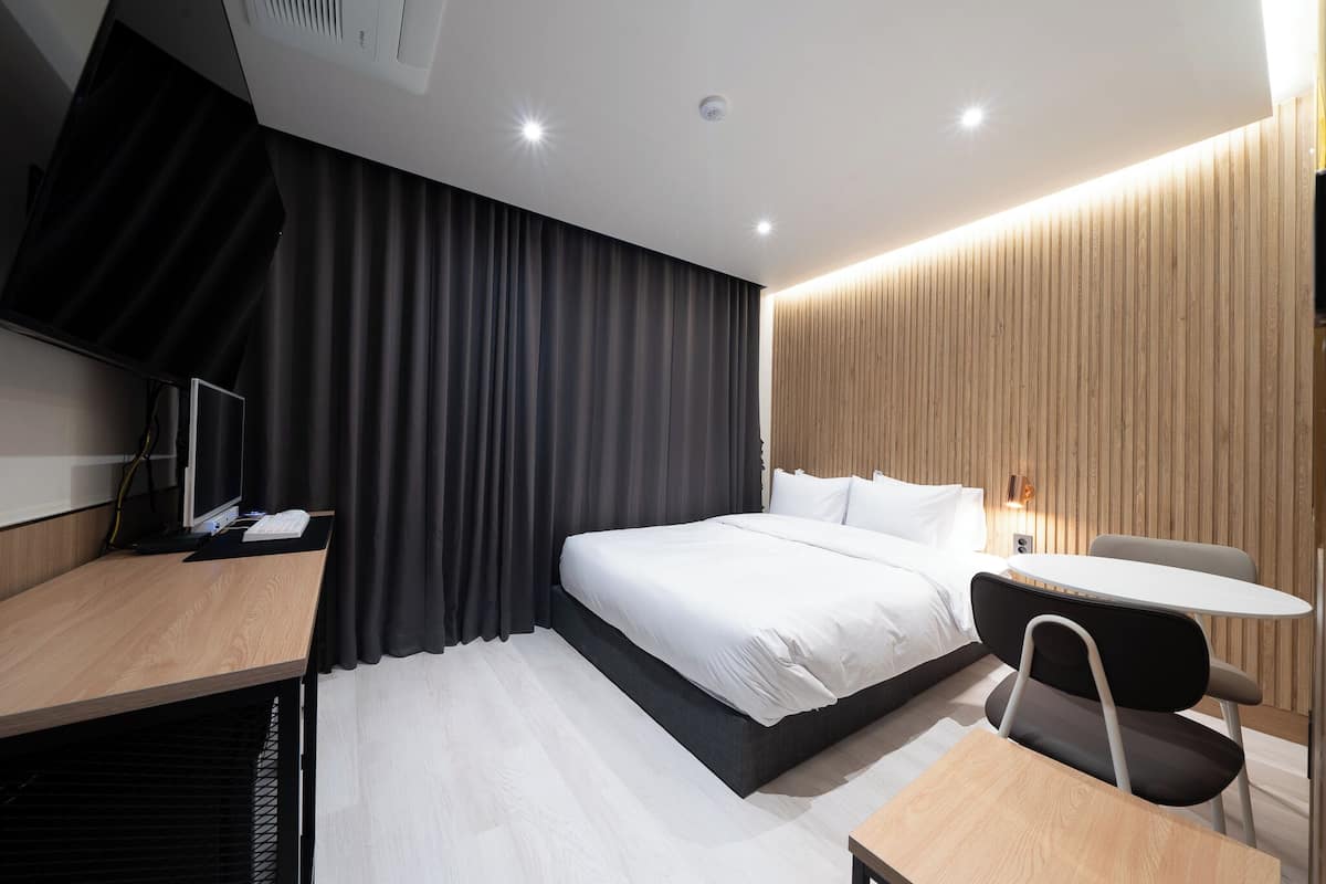 Une chambre d’hôtel moderne avec un grand lit, un bureau équipé d’un ordinateur, une petite table et une chaise.