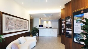 Ein Hotel-Empfangsbereich im modernen Stil, mit einer Rezeption, einem großen gerahmten Kunstwerk an der Wand und einer Sitzecke mit einer weißen Couch.