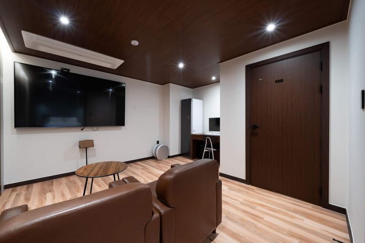 Une chambre moderne dotée d’un grand téléviseur à écran plat, d’une petite table ronde et d’un coin salon avec deux fauteuils.