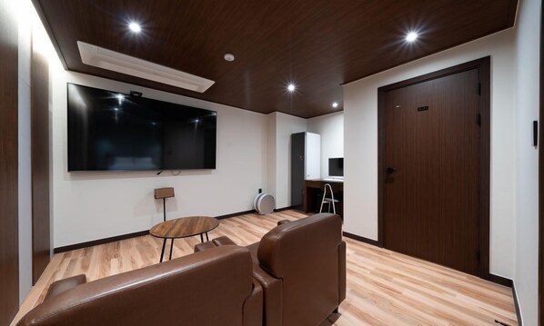 A modern room with a large flat-screen TV, a small round table, and a seating area with two chairs. - Gapyeong hotel GRAZIE (Gapyeong)