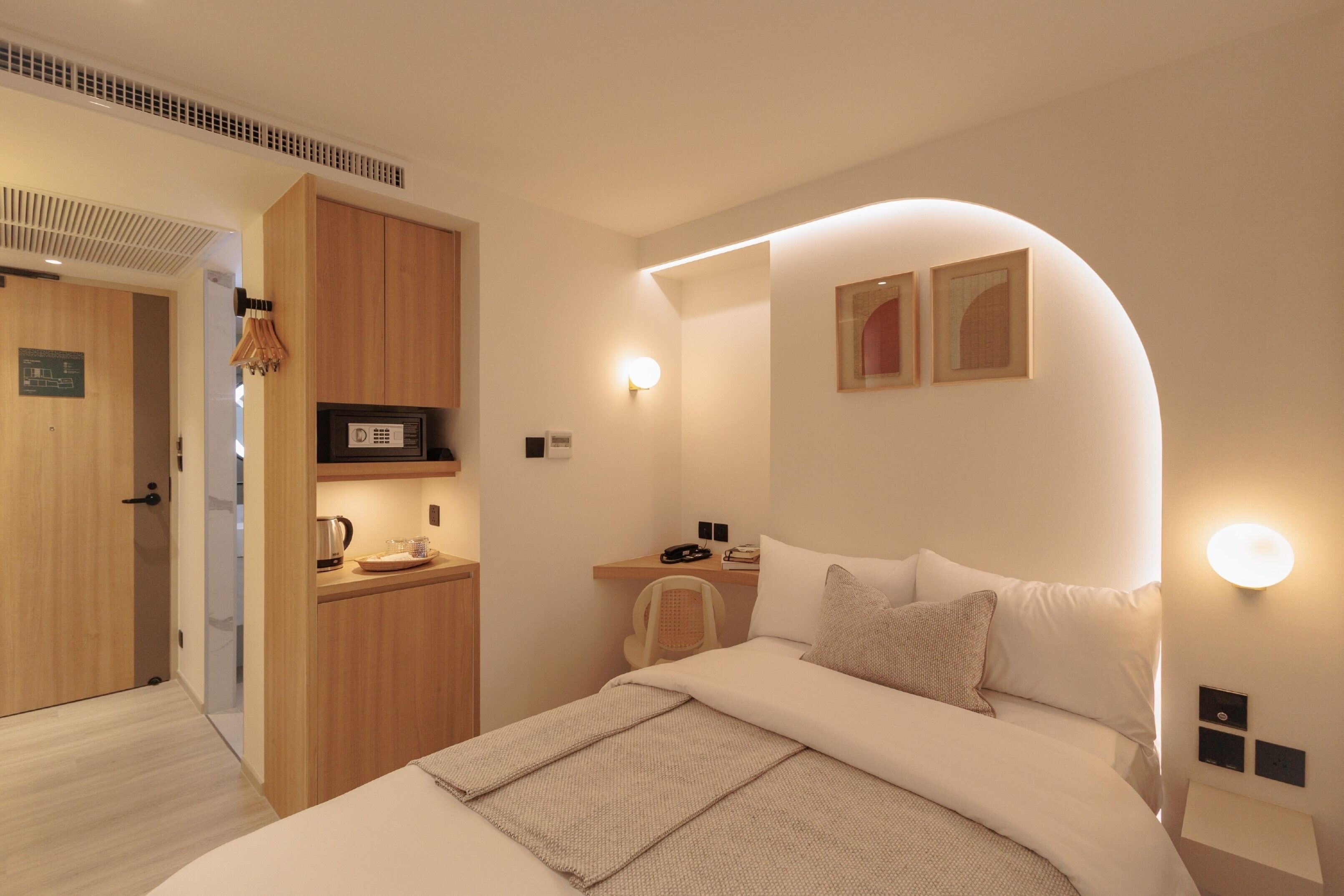 Ein modernes Hotelzimmer mit Bett, Nachttisch und einer kleinen Küchenzeile.