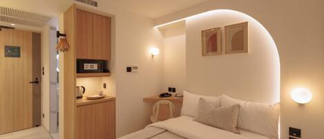 Ein modernes Hotelzimmer mit Bett, Nachttisch und einer kleinen Küchenzeile.