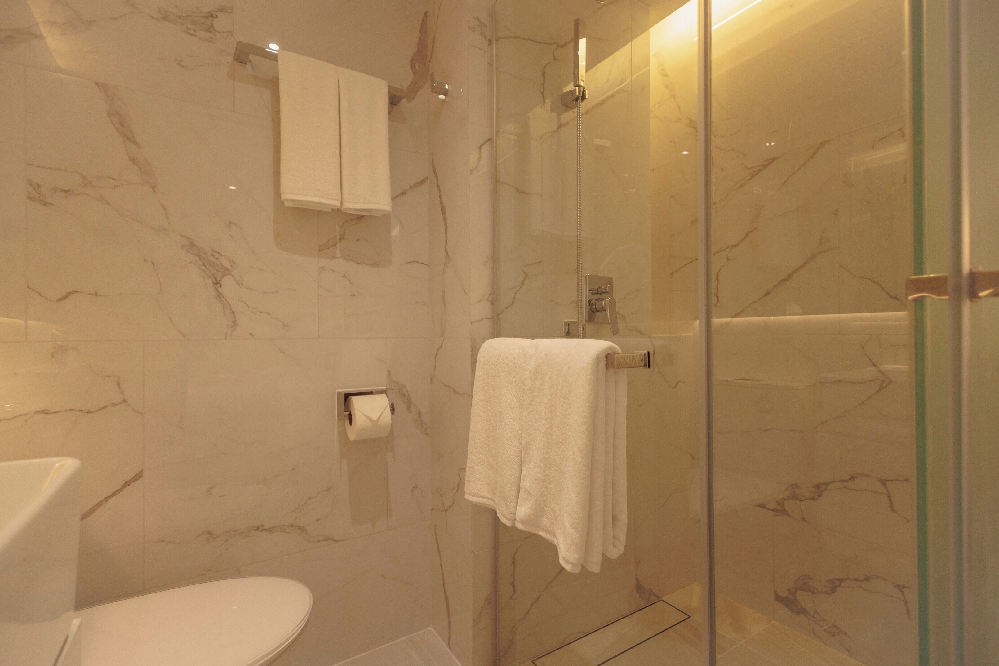 A bathroom with a toilet, a glass shower enclosure, marble walls, and a towel rack.