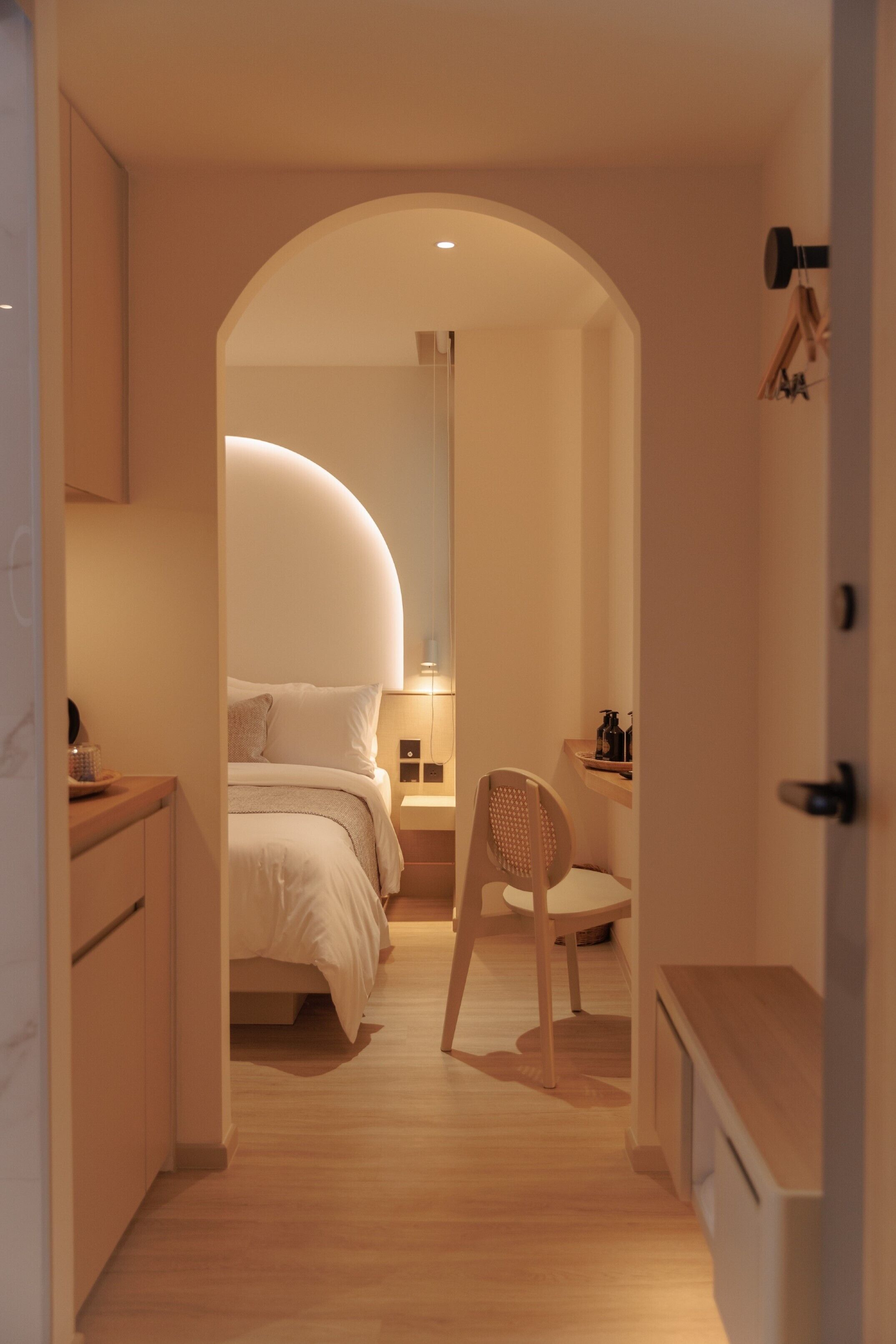 A narrow hallway leading to a bedroom with a curved ceiling, a wooden chair, a bedside table, and a nightstand.