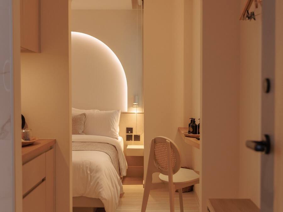 A narrow hallway leading to a bedroom with a curved ceiling, a wooden chair, a bedside table, and a nightstand.
