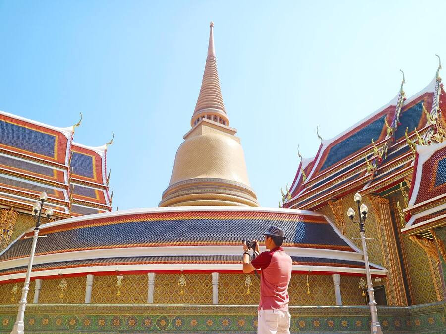 A large temple with a tall spire, ornate decorations, and a person taking a photo.