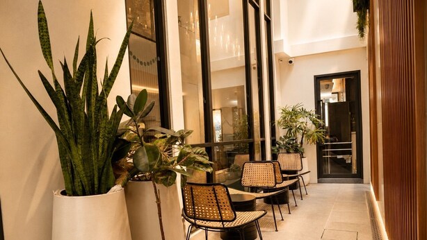 A corridor with potted plants, wicker chairs, and a glass door leading to a room. - Corridor2407 Hotel (Bangkok)