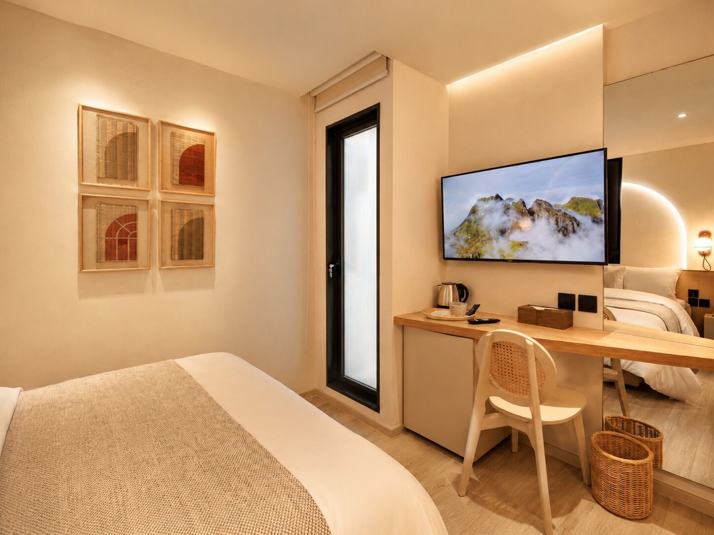 A hotel room with a bed, a desk with a chair, a television, and framed pictures on the wall.