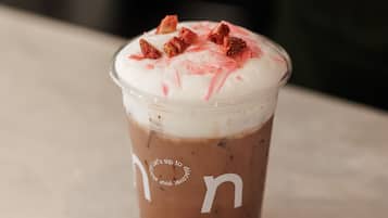 A clear plastic cup with a lid, containing a layered beverage with a whipped topping and a spoon inside.