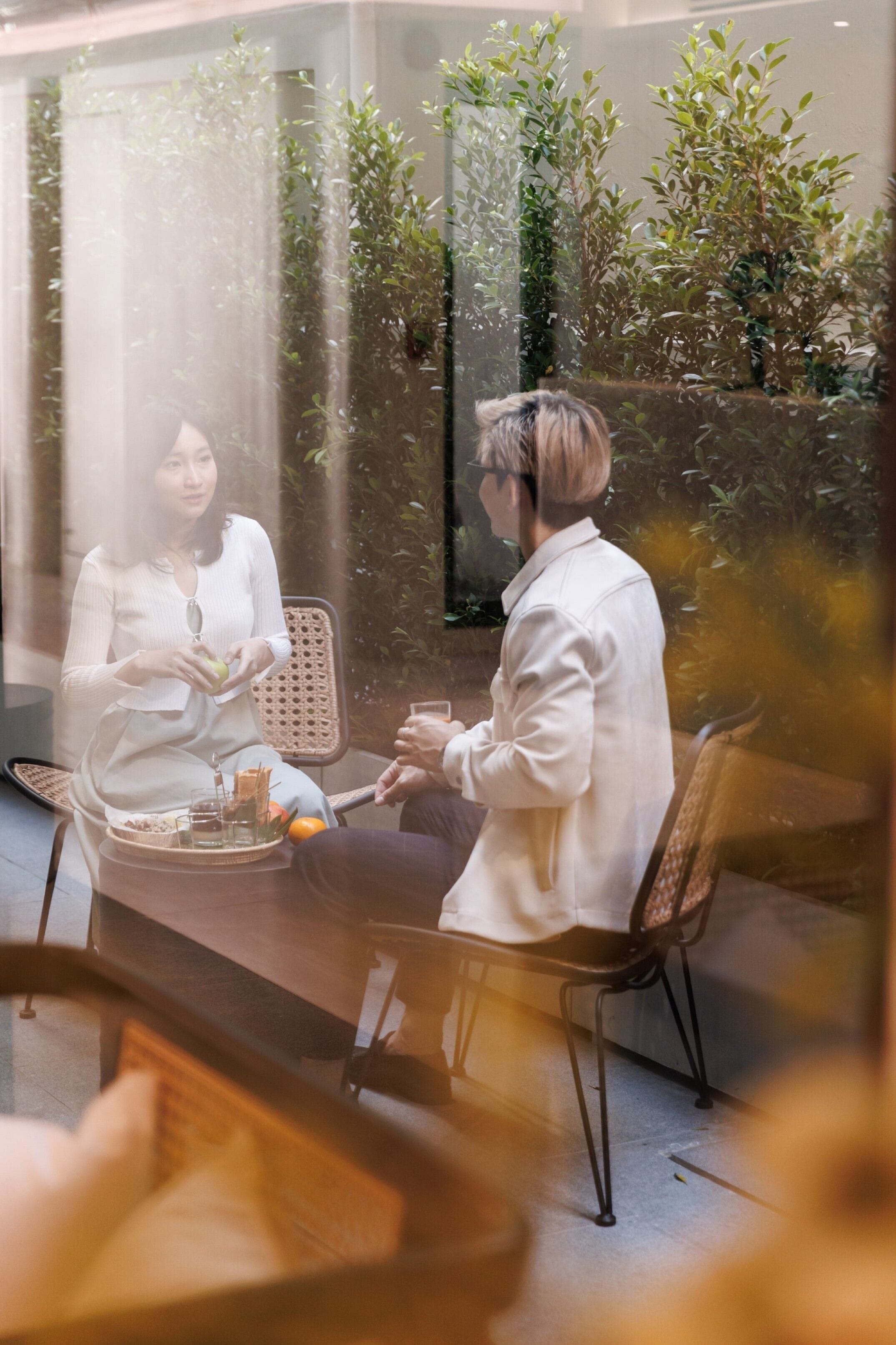 A couple sitting at a table with a glass of wine, surrounded by indoor plants.