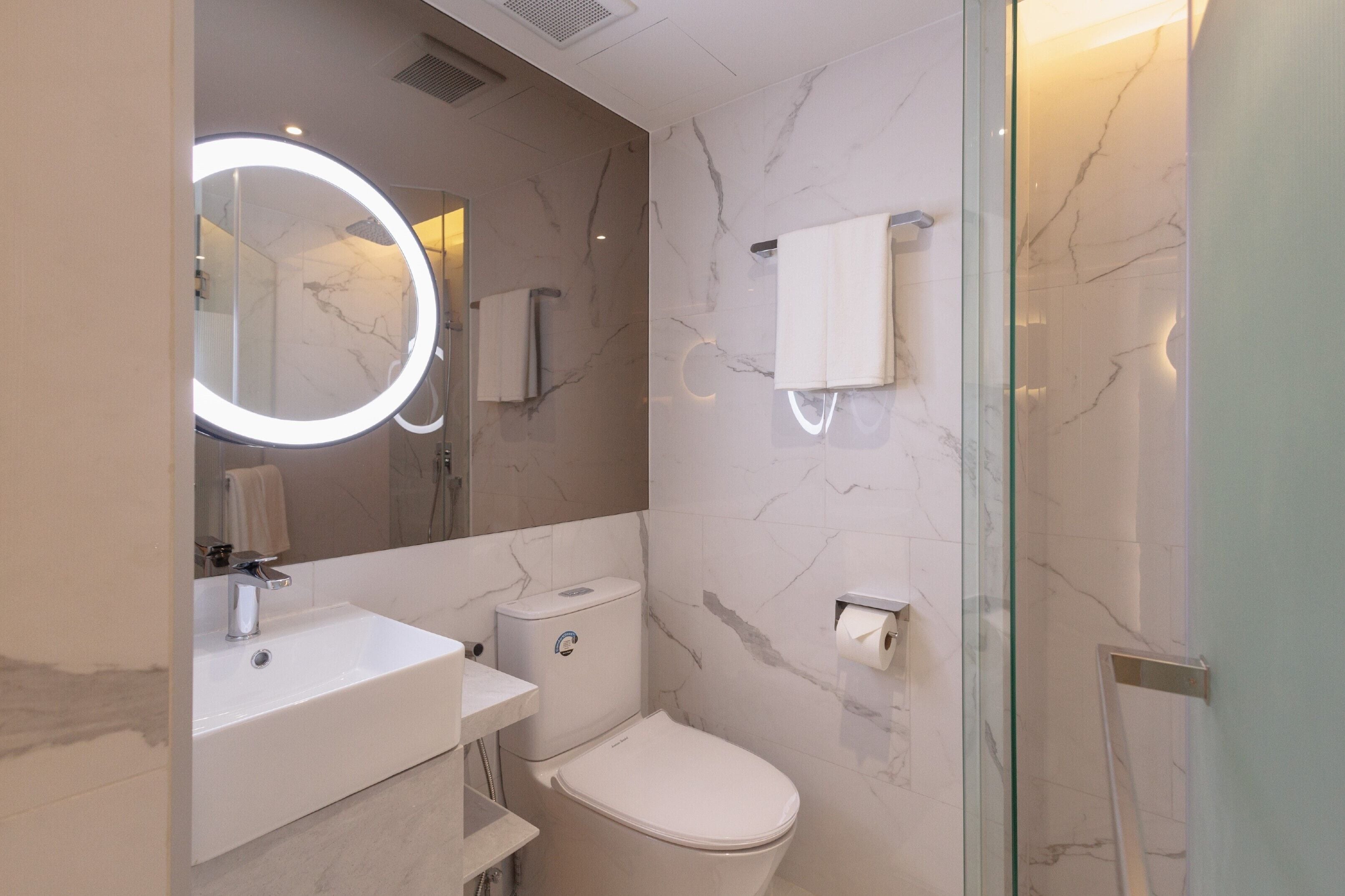 A modern bathroom with a round mirror, a sink, a toilet, and a glass shower enclosure.