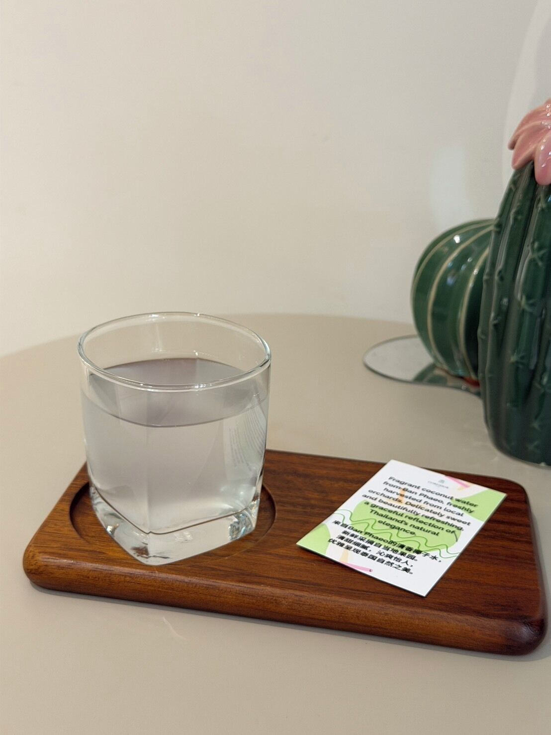 A glass of water on a wooden coaster with a card beside it.