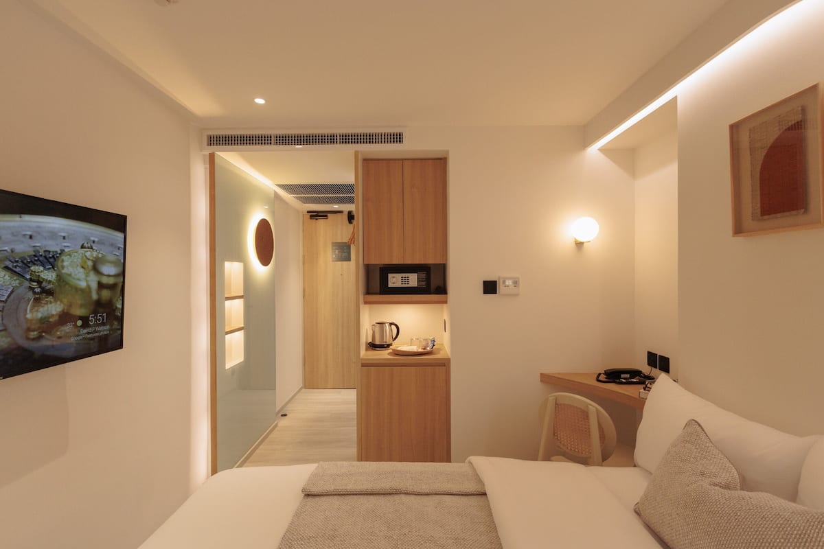 A compact hotel room with a bed, a small kitchenette, a desk, and a chair.