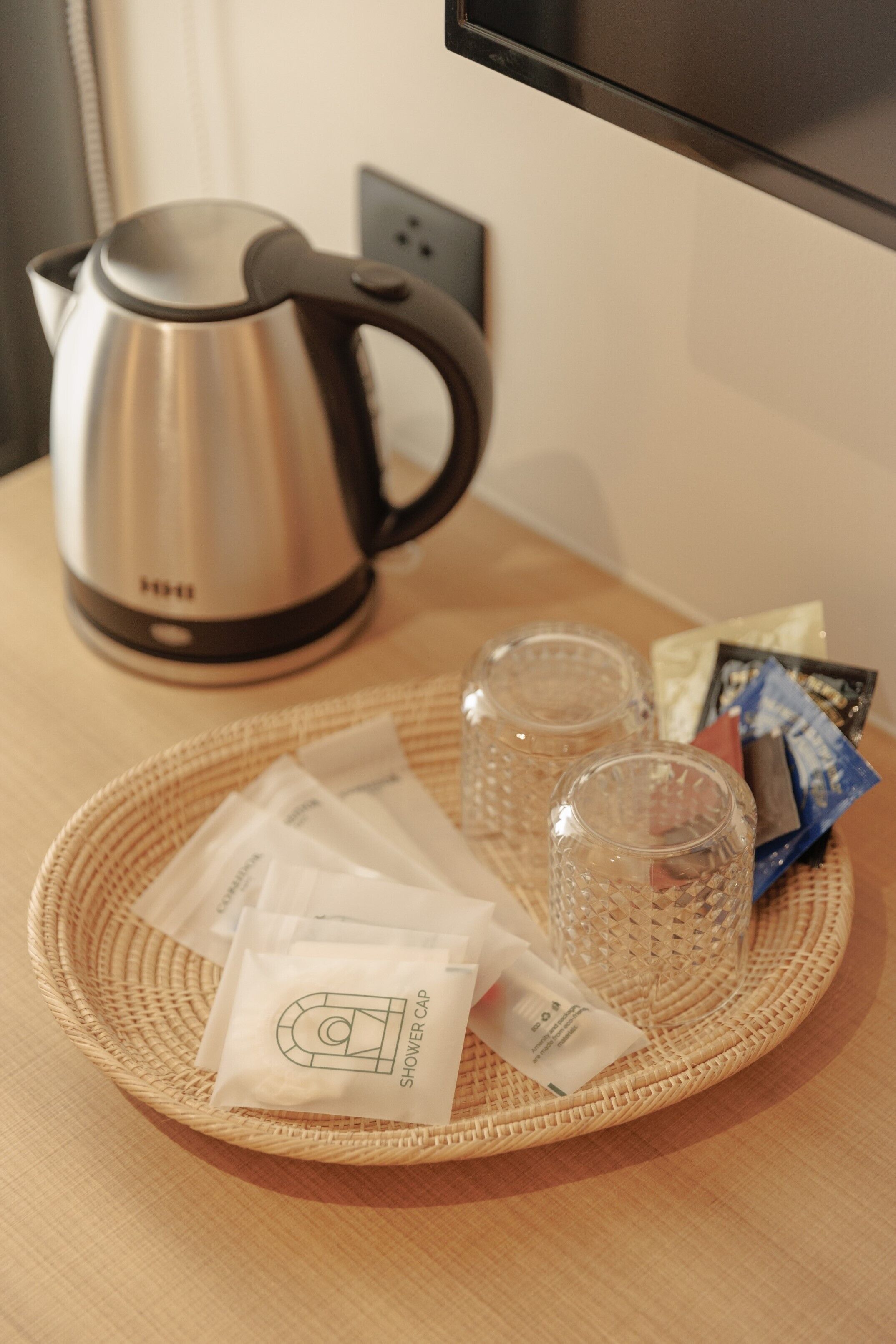 A kitchen area with a kettle, a woven placemat, and toiletries on a table.
