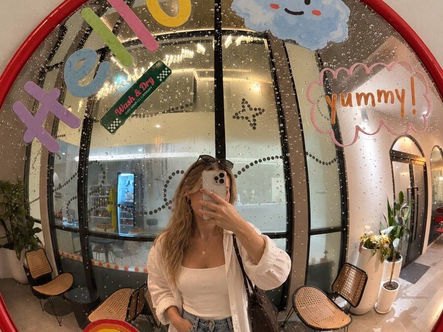 A person taking a selfie in a room with a large mirror reflecting a cafe interior, a rainbow sticker, and a cloud sticker.